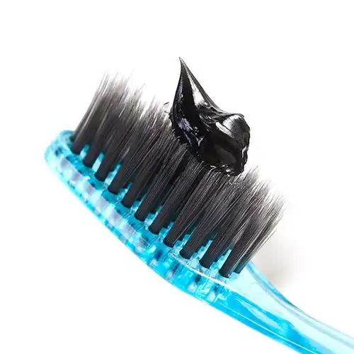 Black activated charcoal toothpaste squeezed onto an eco-friendly bamboo toothbrush, demonstrating natural whitening formula from leading private label OEM manufacturers like Guangzhou Toothpaste Factory