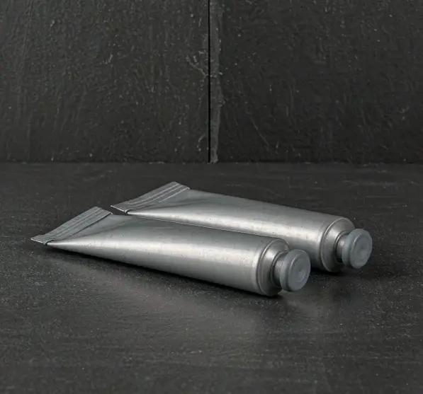 Plain silver aluminium toothpaste tubes with crimped tails on a dark surface